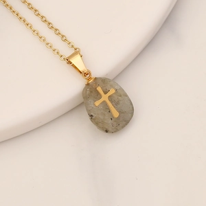 Close-up of a grey oval stone pendant featuring a golden cross on a gold chain