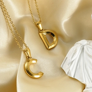Detail of 18K gold-plated C and D letter pendants on elegant silk with a statue background