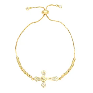 Gold adjustable cross and heart bracelet with cubic zirconia inlays on white background