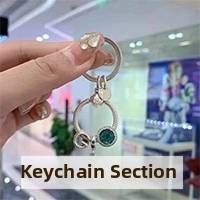 Detail of silver keychain with green gemstone pendant and metallic charms in hand