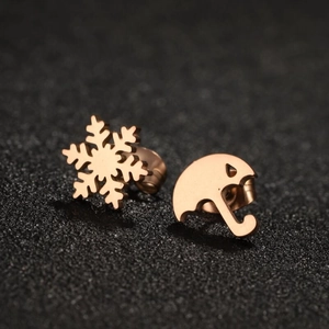 Rose gold asymmetrical snowflake and umbrella stud earrings on a dark textured surface