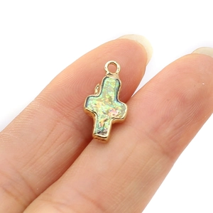 Pendentif croix plaqué or avec incrustation d'opale verte tenu par les doigts