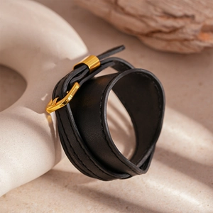 Detail of black leather wrap bracelet with golden metal buckle on warm wood background