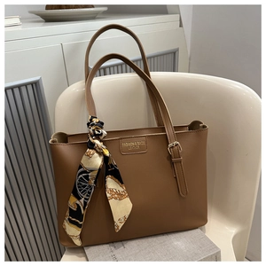 Nahaufnahme einer braunen Leder-Tote-Bag mit goldener Hardware und bedrucktem Seidenschal