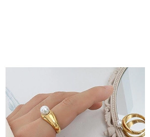 Detailed view of a gold-plated ring with a white pearl inlay on a female finger