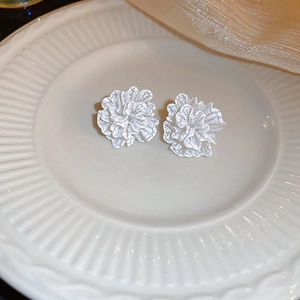 Macro view of white floral stud earrings with textured petals on a ceramic plate