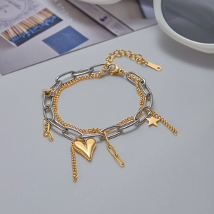 Detail of a layered bracelet with gold heart and star charms on a silver paperclip chain