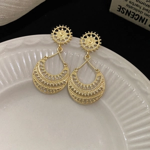 Close-up of golden geometric earrings with teardrop filigree on a ceramic tray