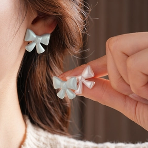 Close-up of pastel acrylic bow earrings with pearl luster on a model's earlobe