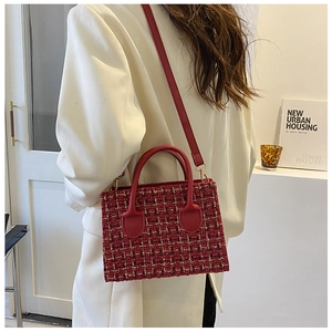 Detail of red checkered tweed handbag featuring a leather handle and adjustable shoulder strap