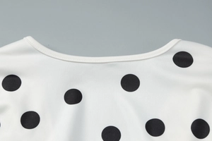 Dettaglio dello scollo profondo a V sul vestito bianco con motivo a pois neri chic