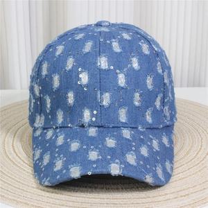 Detailed view of blue denim baseball cap with sequin accents and distressed hole design