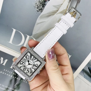 Detalle de un reloj cuadrado plateado con bisel de pedrería y grandes números arábigos