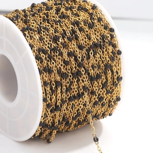 Close-up of golden stainless steel chain with black enamel beads on a white spool