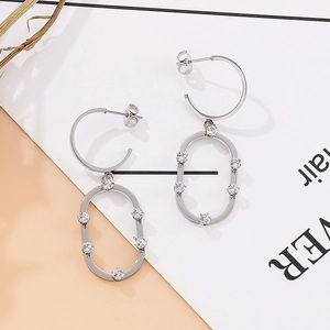 Détail de boucles d'oreilles ovales argentées avec zircons sur un fond minimaliste