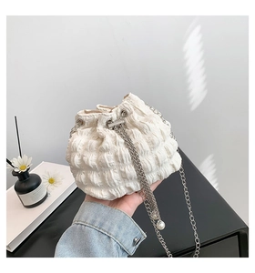 Detailed shot of a white pleated bucket bag featuring silver chain and pearl drawstrings