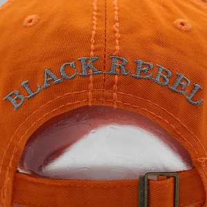 Detail of orange cotton baseball cap featuring BLACK REBEL embroidery and metal buckle