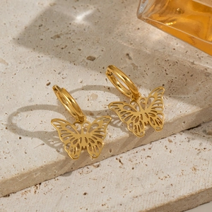 Macro detail of gold butterfly drop earrings with delicate cutout design on stone