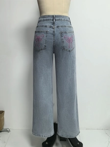 Detail van roze strikborduurwerk op de achterzak van de wijde denim broek
