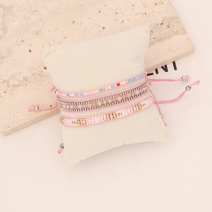 Detail of bohemian multilayer beaded bracelet set with pink woven cord and golden beads