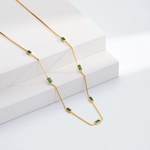 Detail of gold box chain necklace featuring rectangular emerald green stones on stone pedestal