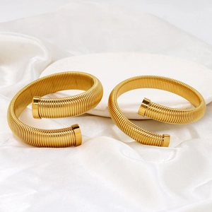 Close-up of golden spiral spring open cuffs on a white silk and marble background