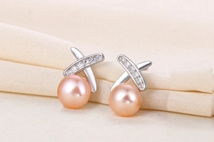 Macro shot of silver X-shaped earrings with sparkling zircon and pink freshwater pearls