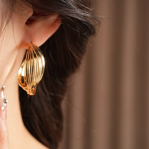 Close-up of model wearing gold multilayered hoop earrings with a textured twist finish