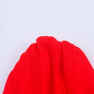 Détail de la robe midi plissée rouge montrant la texture translucide et la lumière douce