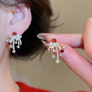 Macro shot of gold plated firework earrings with red gems and pearls on ear