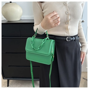 Detail of a green crossbody bag with a thick chain strap and top handle on a model