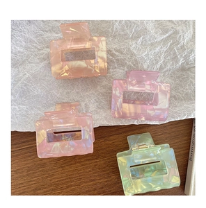 Detail view of pink and green iridescent square claw clips on a stylish aesthetic background