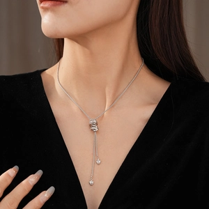 Detail of silver Y-shaped necklace with zircon knot pendant and heart charms on model