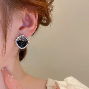 Close-up of square stud earring with dark resin center and shimmering crystal border