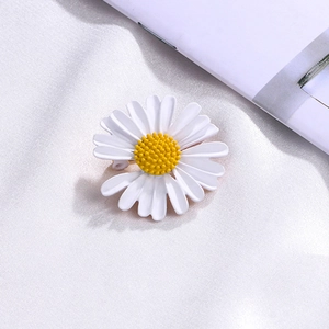 Macro shot of white enamel daisy brooch with yellow core on white silk fabric