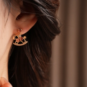 Close-up of gold rocking horse earring with red patterns and cubic zirconia on ear