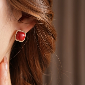 Close-up of a gold square earring with red gemstone and diamonds on a female model's ear