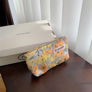 Detail of floral jacquard mini makeup bag with metal zipper on a rustic wooden surface