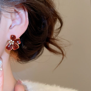 Detail of red flower stud earring with gold edges and zircon center on model