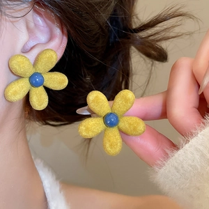 Detail of yellow flocked flower earring with blue center bead worn by model