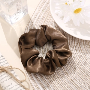 Lustrous brown silk satin scrunchie shown in a stylish minimalist lifestyle flatlay