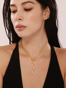 Gros plan du collier nœud doré avec pampilles de perles et boucles d'oreilles assorties