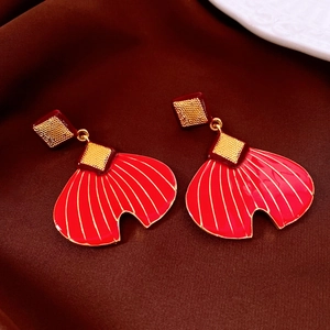 Detail of red fishtail drop earrings with gold textured plating on silk background