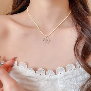Dettaglio della collana di perline con ciondolo a fiore indossata su camicia in pizzo
