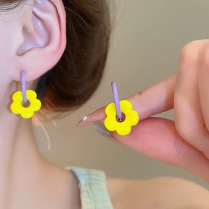 Detailed close-up of yellow flower earrings with purple hoops worn by a model