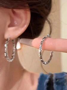 Close-up of large silver hoop earrings with diamond-cut faceted surface on a female model
