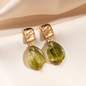 Detail of green waterdrop acrylic earrings with gold square metallic top on silk