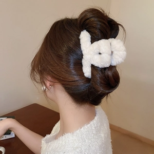 Close-up of white plush cross claw clip worn on hair showing soft faux fur texture