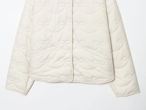Close-up of bow-shaped quilted stitching and buttons on cream lightweight jacket