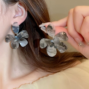 Detailed macro view of large acrylic flower earrings with grey marble texture on model